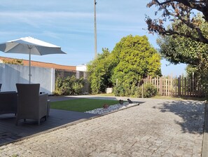 A paved patio with a white umbrella, wicker furniture, a small lawn, and a wooden fence. - Eira da Mila - 2-bedroom house with outdoor area (Coimbra)