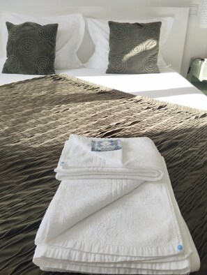 Un lit bien fait, recouvert d’une couverture marron à texture, avec deux oreillers ornés de motifs circulaires et une serviette blanche pliée posée sur le lit.