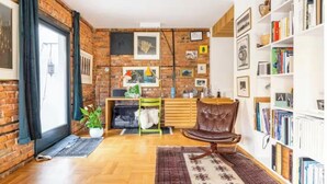 A living room with a brick wall, wooden floor, a leather chair, a bookshelf, and a fireplace.