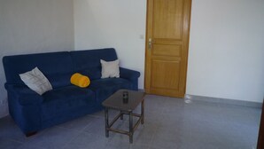 Een kamer met een blauwe bank, een klein houten tafeltje en een houten deur.
