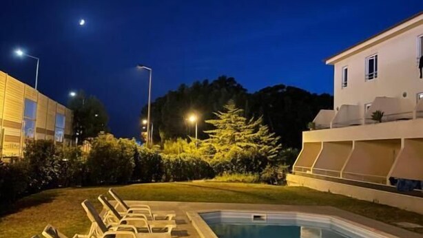 A pool area with lounge chairs and a building in the background. - Juiceven Studios (Cascais)