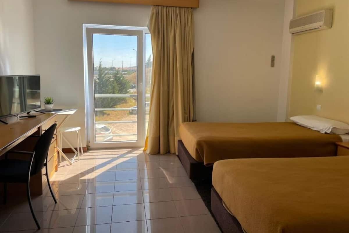 Habitación de hotel con escritorio, dos camas, televisor y vista a través de un ventanal grande.