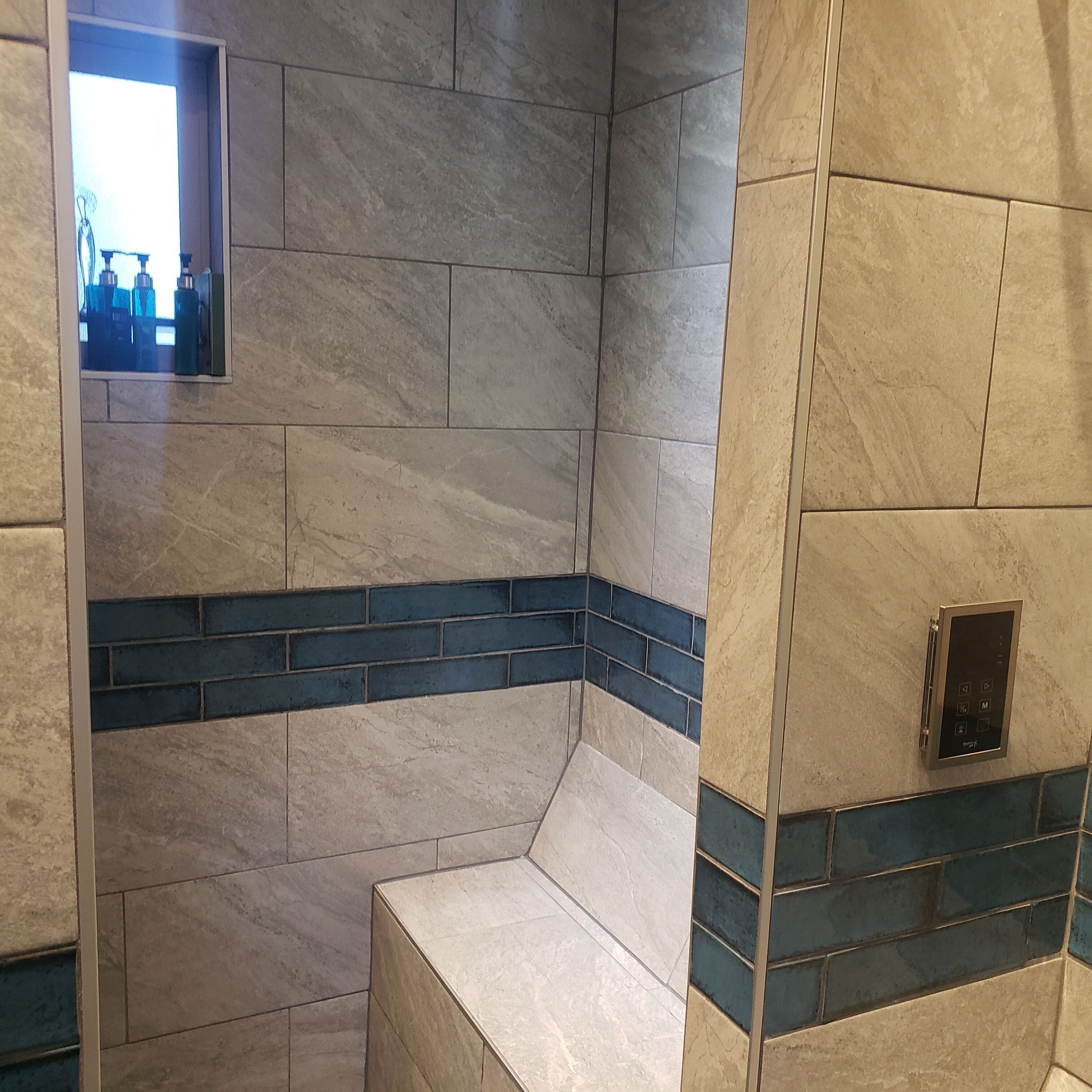 A bathroom with a tiled shower area, a bench, and a control panel.