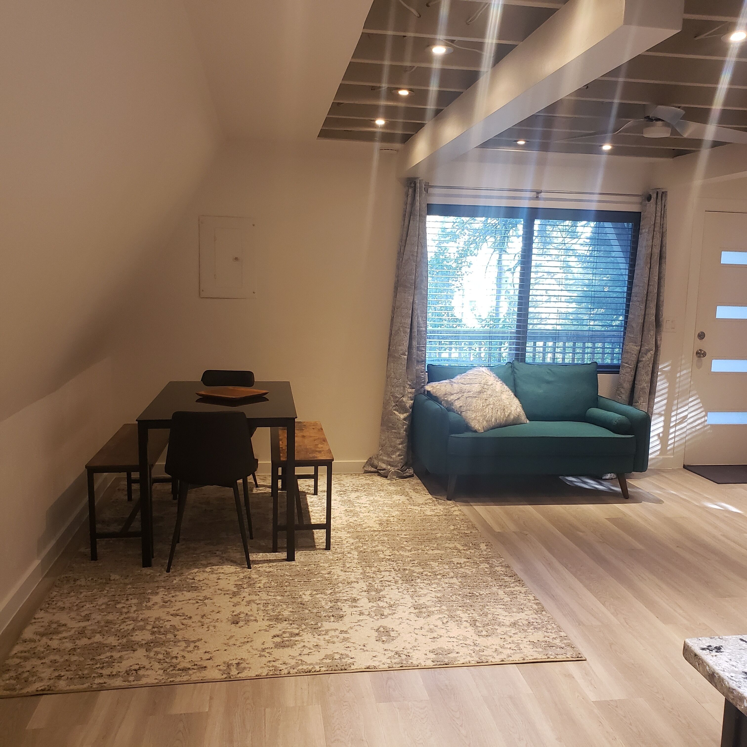 A compact living space with a dining table, a sofa, and a large window with blinds.