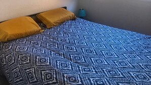 Makuuhuoneessa on sänky, kaksi tyynyä, ikkuna, jossa on sälekaihtimet, ja peili seinällä.