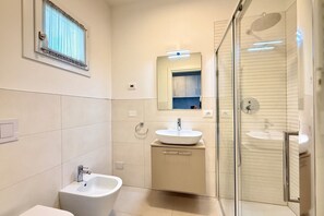 A modern bathroom with a glass-enclosed shower, two sinks, a bidet, and a mirror above the sink. - Meit 5b - Carraro Immobiliare Jesolo (Lido di Jesolo)