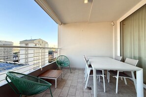 A balcony with a table and chairs, a chair, and a view of buildings. - Meit 5b - Carraro Immobiliare Jesolo (Lido di Jesolo)