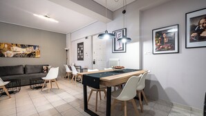 Un'area pranzo moderna con un tavolo di legno, sedie bianche e una tovaglia nera. Sullo sfondo, un divano grigio e un tavolino da caffè nero.