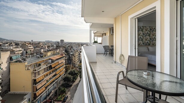 Un balcone con tavolo e sedie in vetro, affacciato su un panorama urbano con diversi edifici.