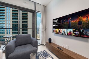 A modern living room with a grey sofa, a coffee table, and a TV wall with movie posters. - Luxury 1BR 5 Min to Burj Khalifa Prime Stay (dubai)