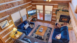 Interior acolhedor de uma cabana com lareira, paredes de madeira, um sofá, uma mesa de centro e uma televisão.