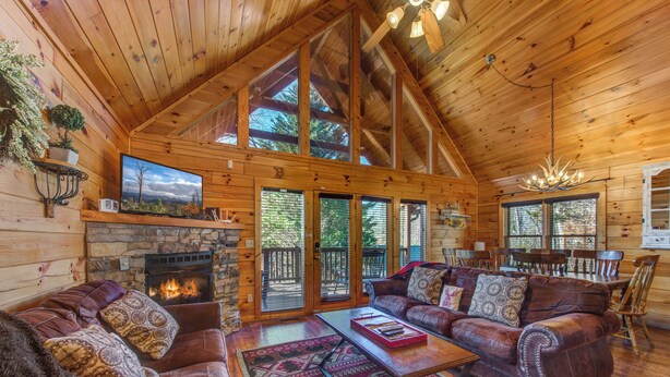 A log cabin interior with a fireplace, leather sofas, a dining area, and large windows. - Cozy 3-bedroom haven for up to 10 guests. (Gatlinburg)