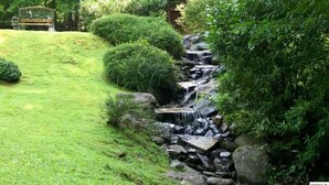 A garden with a small waterfall, a wooden bench, and a wooden fence. - Cozy 3-bedroom haven for up to 10 guests. (Gatlinburg)