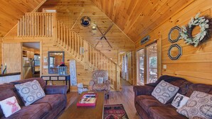 A spacious wooden cabin interior with a living area featuring two leather sofas, a coffee table, and a staircase leading to an upper level. - Cozy 3-bedroom haven for up to 10 guests. (Gatlinburg)