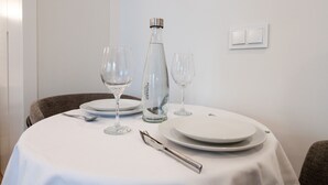 Mesa posta com pratos brancos, duas taças de vinho, uma garrafa de água e um garfo de prata.