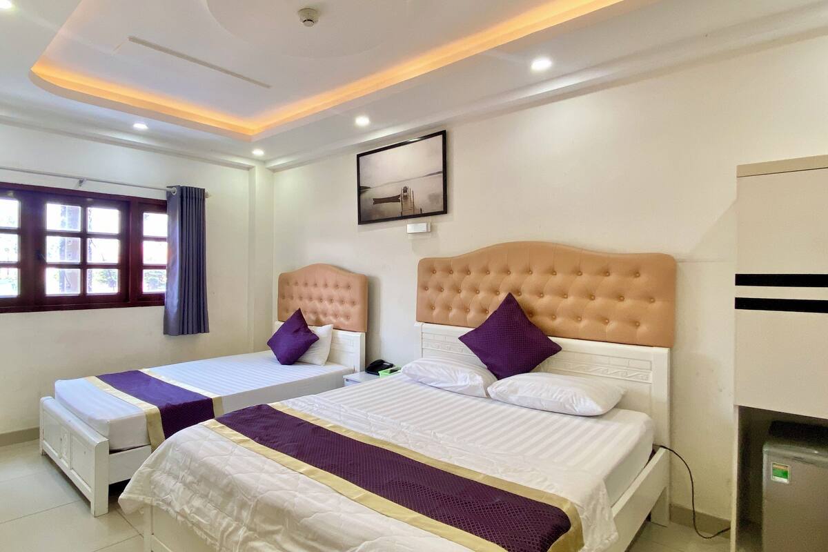 A hotel room with two beds, a ceiling light fixture, a window with curtains, and a wall-mounted picture.