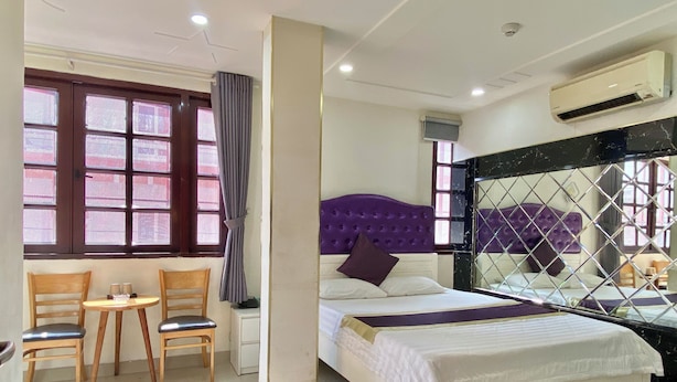 Camera d'albergo con un letto, un tavolino con sedie, una finestra con tende e un condizionatore d'aria.