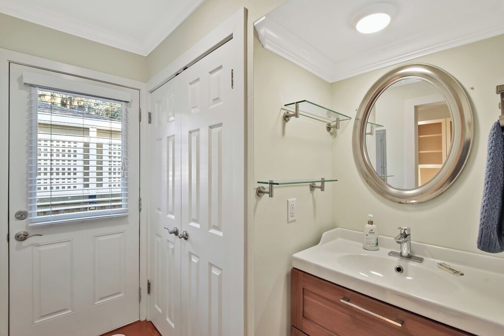 A bathroom with a white vanity, a round mirror, and a glass shelf.