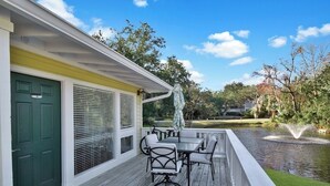 A covered outdoor deck with a table and chairs, a green door, and a view of a pond with a fountain. - 2 bedroom 2 bath condo with deck overlooking lagoon. (Saint Simons Island)