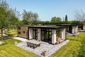 A modern, single-story building with large glass doors, a patio with outdoor furniture, and a surrounding grassy area.