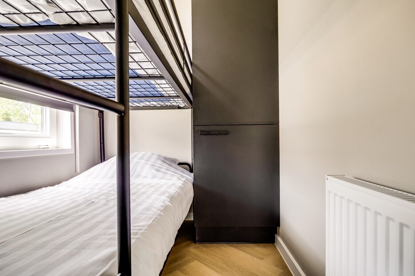 A compact room with a bunk bed, a small refrigerator, and a window with a view of the outside.