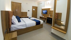 Habitació d'hotel moderna amb un llit de fusta, un escriptori amb un ordinador, una televisió i un gran mirall.