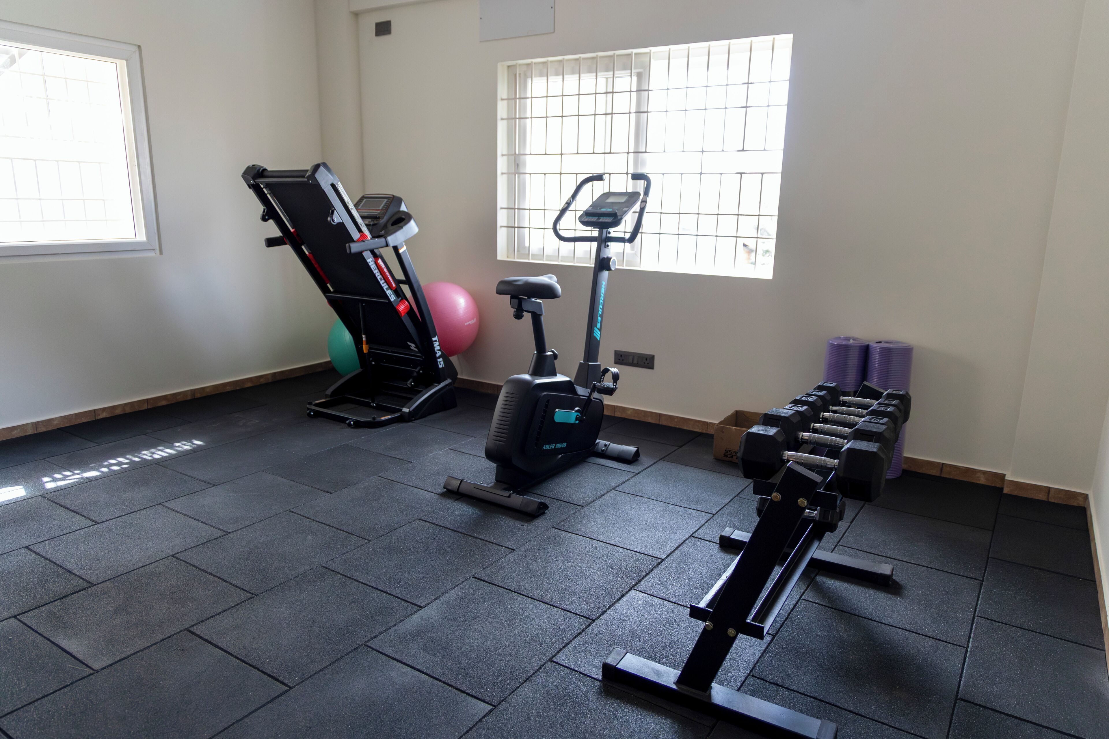 A gym with exercise equipment, a window with bars, and a pair of dumbbells.