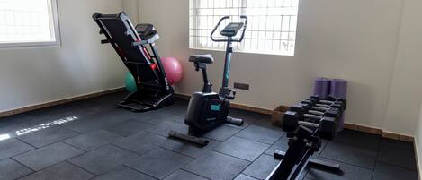 A gym with exercise equipment, a window with bars, and a pair of dumbbells.