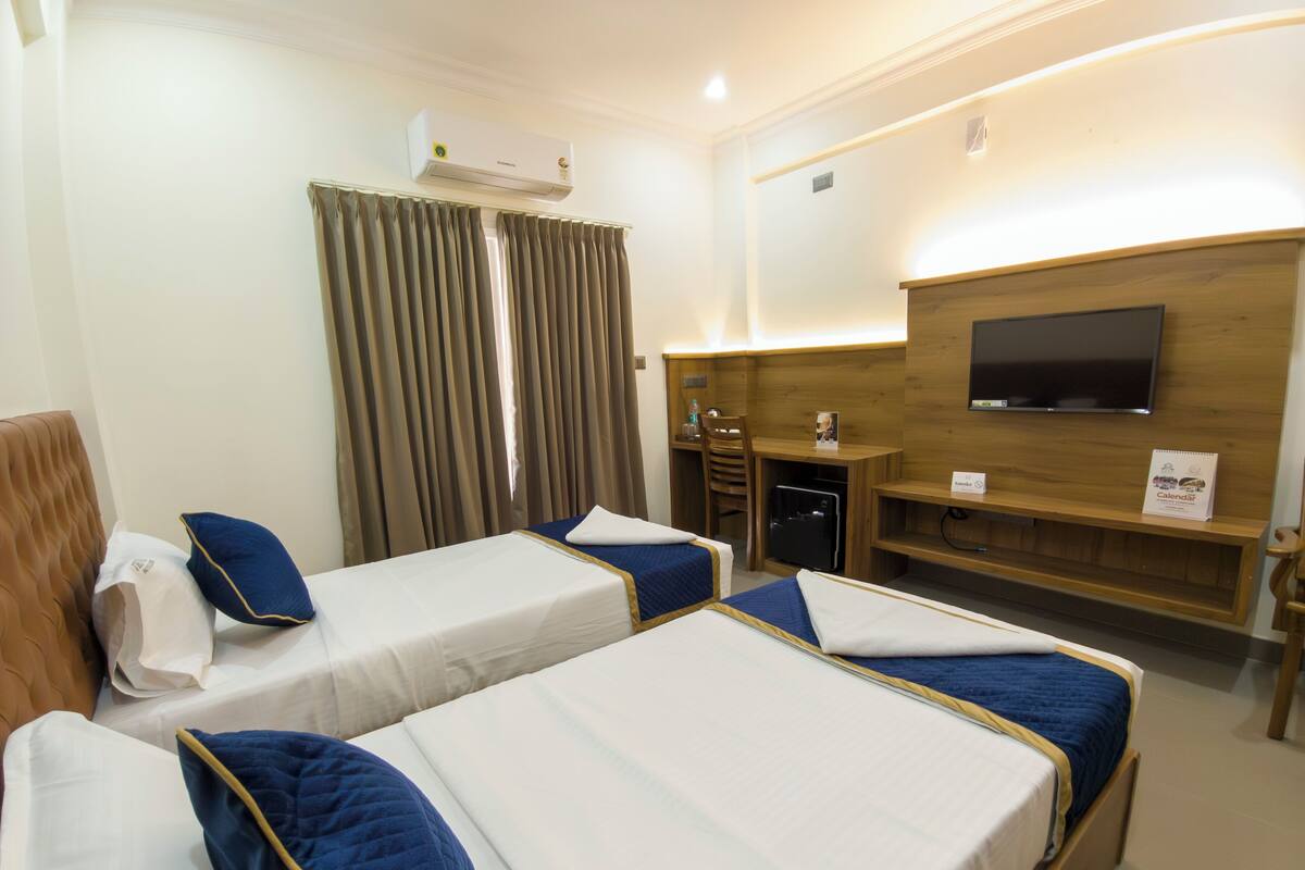 Camera d'albergo con due letti, una scrivania, una sedia, una TV e un condizionatore d'aria.