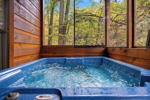 A hot tub with a view of a forest through a window. - Authentic Log Cabin with Game Room (GATLINBURG)