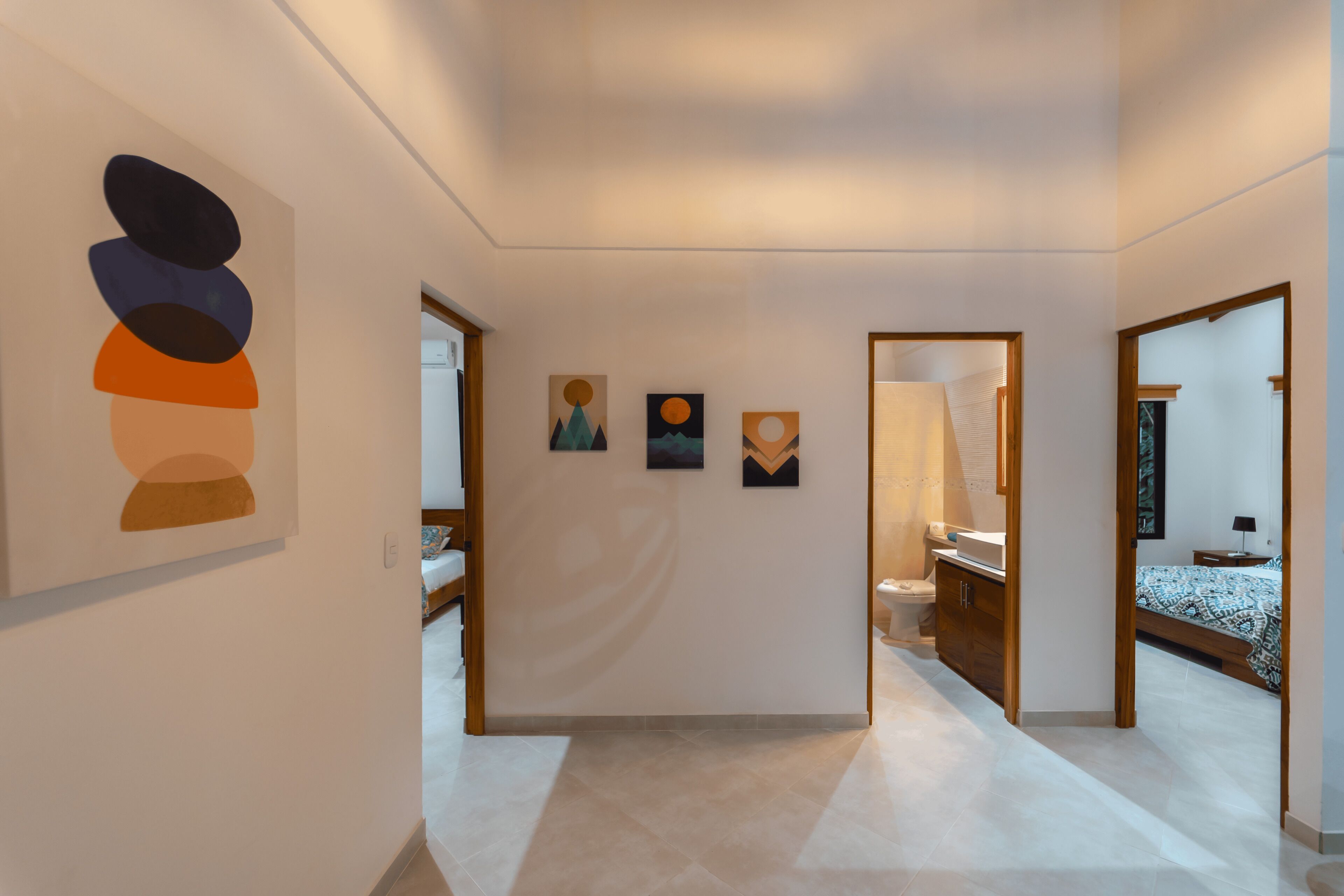 En modern hotellkorridor med en minimalistisk design, med en stor, abstrakt målning på vänster sida, en serie mindre konstverk på väggen och en väl upplyst interiör där badrummet och sovrummet syns.