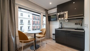 A compact kitchen with a microwave, sink, and knife set. There is a round table with two chairs and a window with a view of buildings. - 302 — SB20 Boutique Studios | 1BR | 1BA | W/K (Madrid)