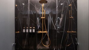 A modern shower with a golden showerhead and control panel, set in a black marble bathroom with glass doors. - 302 — SB20 Boutique Studios | 1BR | 1BA | W/K (Madrid)
