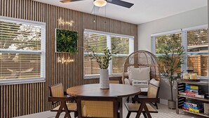 A dining area with a round table, four chairs, a ceiling fan, and a bookshelf with board games. - Right at Home Stays - Entire Home in Pinellas Park (Pinellas Park)