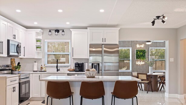A modern kitchen with white cabinets, stainless steel appliances, and a central island with bar stools. - Right at Home Stays - Entire Home in Pinellas Park (Pinellas Park)