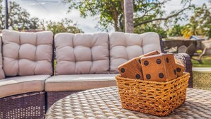 A wicker basket with wooden dice on a woven table, placed on a curved sofa with cushioned seats. - Right at Home Stays - Entire Home in Pinellas Park (Pinellas Park)