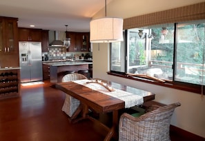 Una cocina moderna con una isla grande, electrodomésticos de acero inoxidable y un comedor con sillas de mimbre y una mesa de madera.