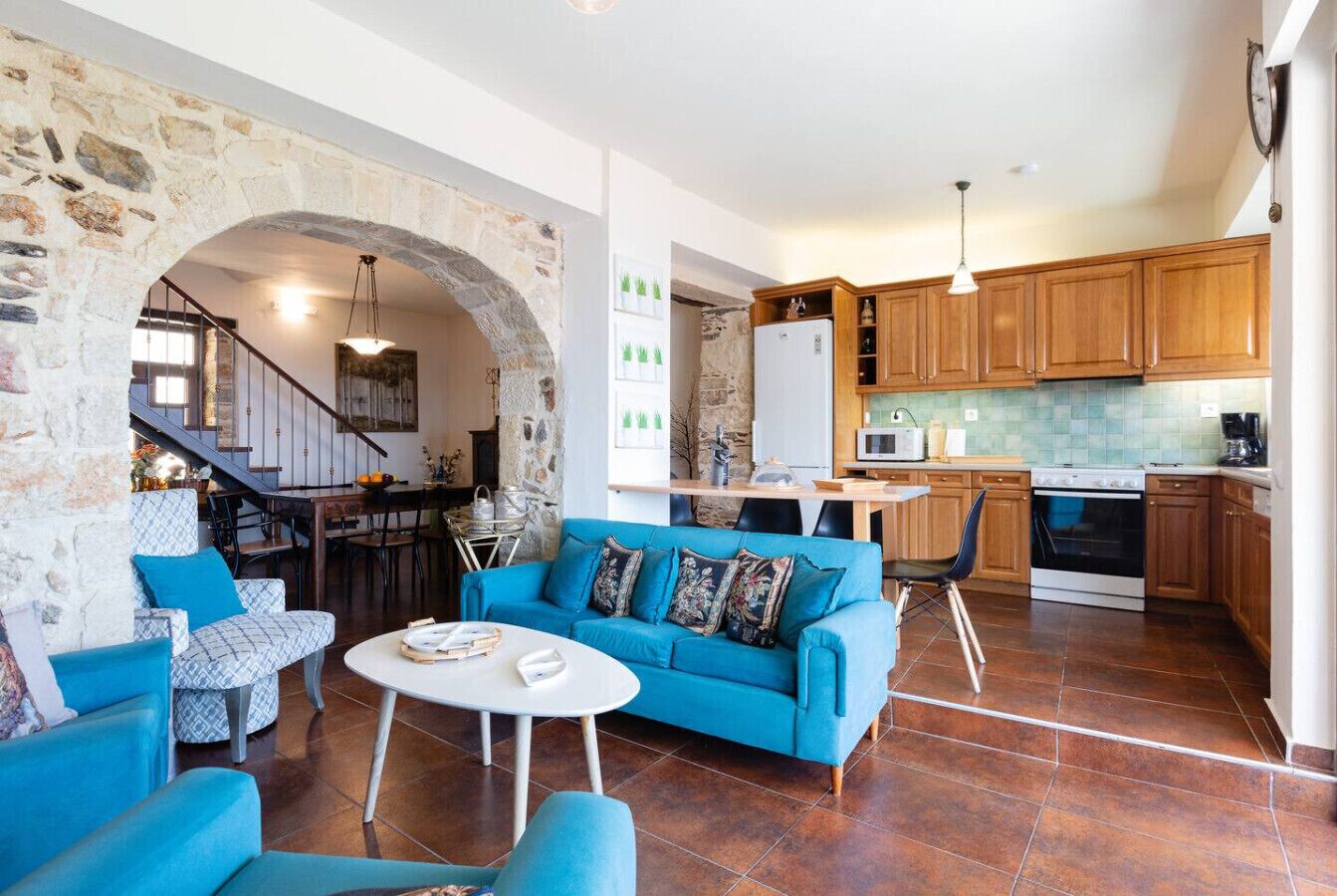 Amplia sala de estar con un sofá azul, una mesa de comedor y una cocina al fondo.