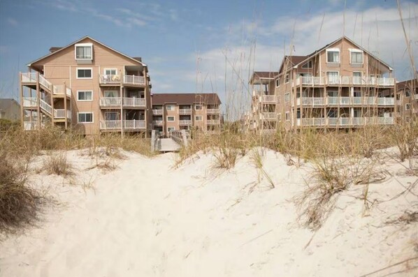 A beachfront hotel with multiple floors, balconies, and a sandy beach area. - 2-Bed 2-Bath Oceanfront Condo in Carolina Beach with 2 Pools and Beach Access! (Carolina Beach)
