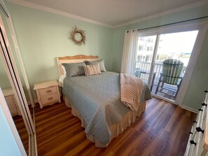 A bedroom with a bed, a nightstand, a dresser, and a balcony with a view. - 2-Bed 2-Bath Oceanfront Condo in Carolina Beach with 2 Pools and Beach Access! (Carolina Beach)