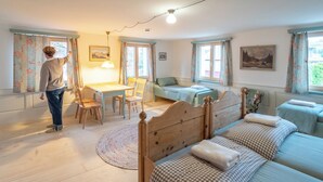 Ein gemütliches Schlafzimmer mit einem hölzernen Bett, einem kleinen Schreibtisch und einem Stuhl. Es gibt zwei Fenster mit Vorhängen, eine Lampe und ein Bild an der Wand.