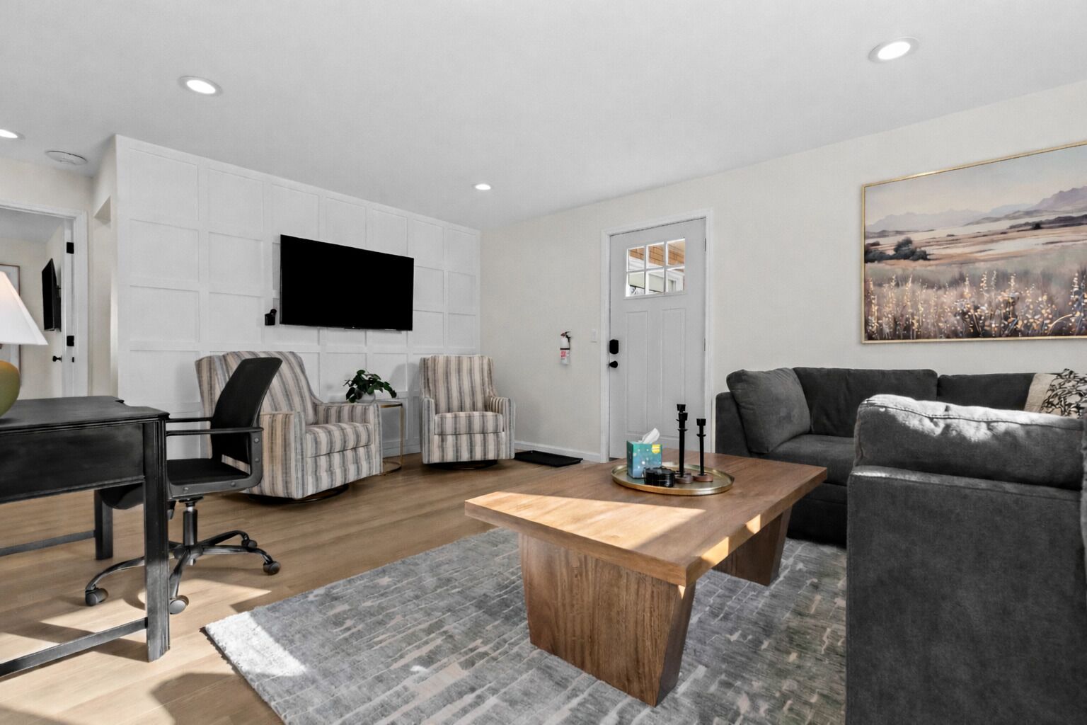 Ein modernes Wohnzimmer mit einem Flachbildfernseher, zwei gestreiften Sesseln, einem grauen Sofa, einem Holztisch und einem Bild an der Wand.