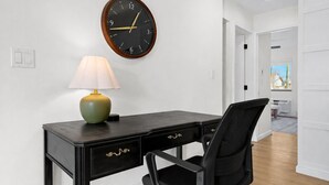 Een kamer met een bureau, een stoel, een wandklok en een lamp.