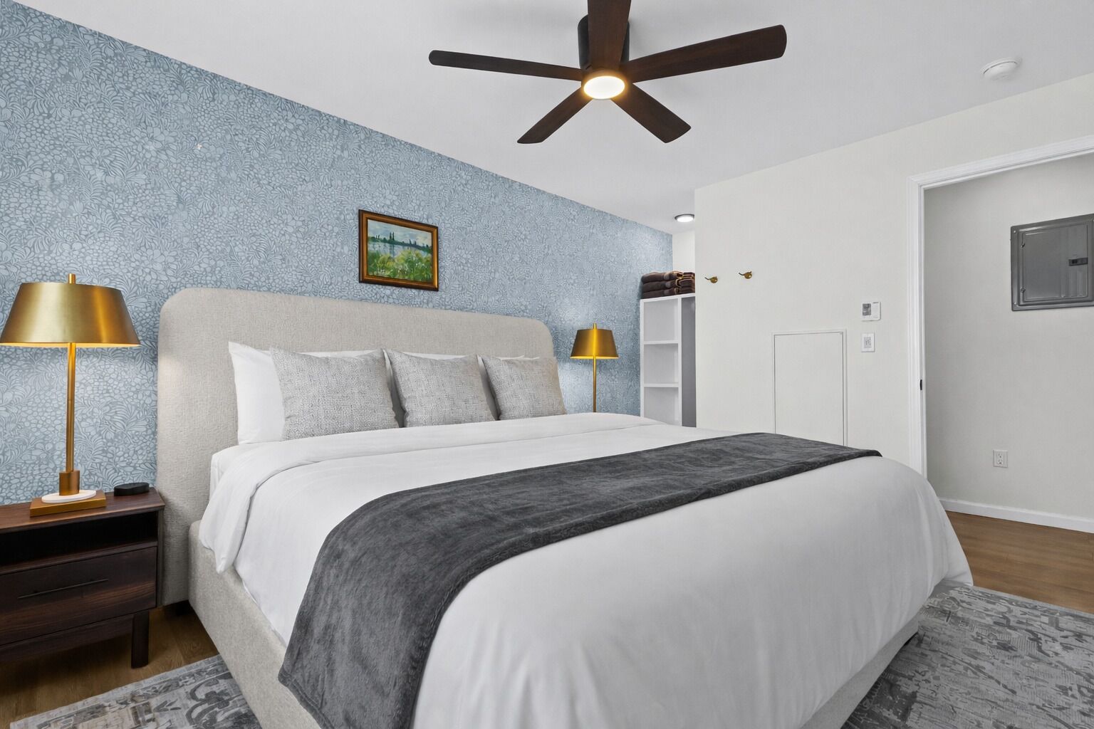 Ein Schlafzimmer mit einem Bett, zwei Nachttischlampen, einem Deckenventilator, einem Bild an der Wand und einem Kleiderschrank.