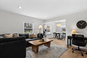 A modern living room with a sofa, coffee table, and a dining area with chairs and a table. - New! Luxury 2BR Suite | 20 min to Downtown Detroit (Eastpointe)