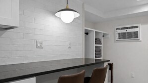 Una cocina moderna con azulejos blancos tipo metro, encimera negra, dos sillas marrones, una lámpara colgante y un estante empotrado con toallas.