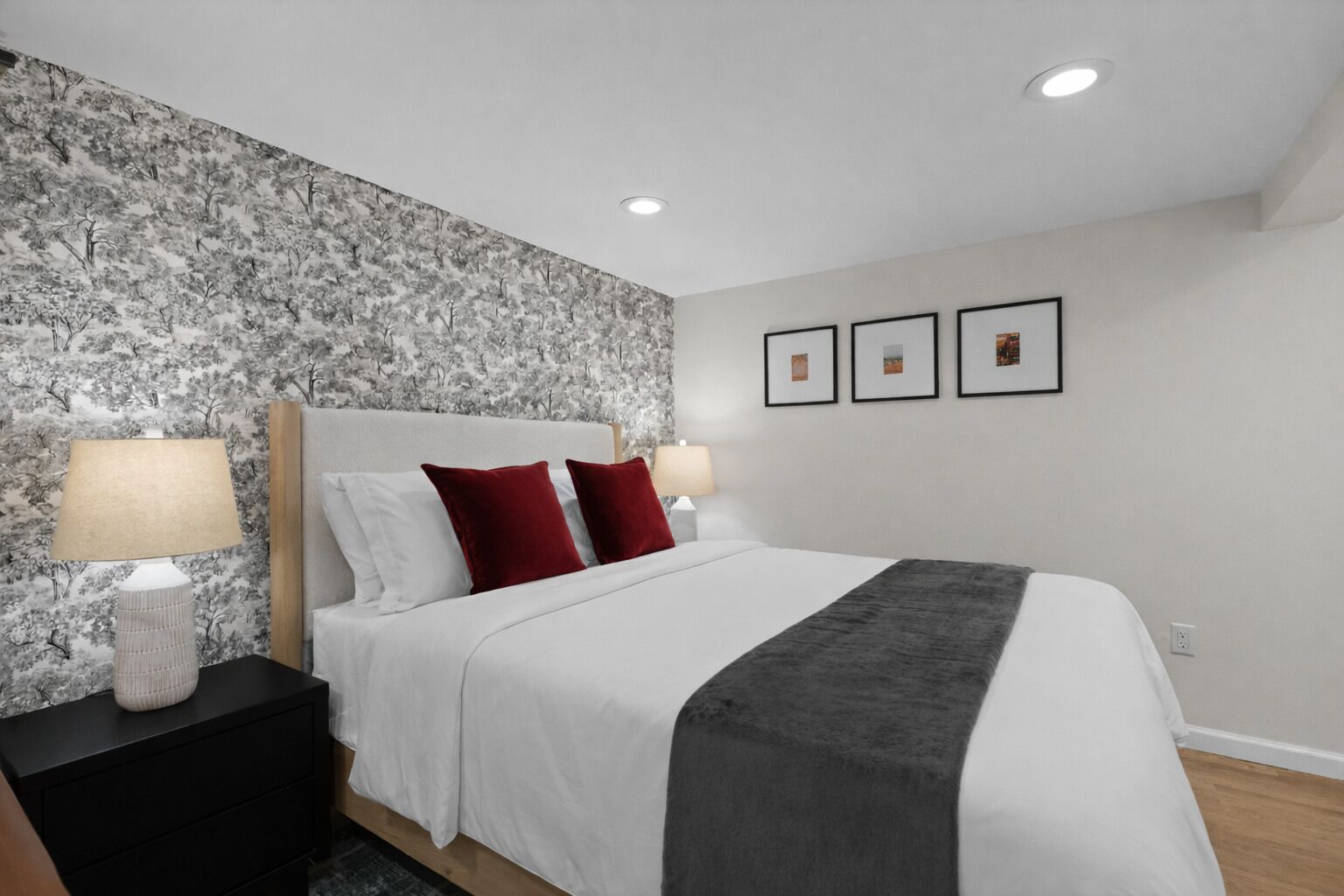 Une chambre à coucher comprenant un lit, deux tables de chevet, une tête de lit et un mur orné de trois tableaux encadrés.
