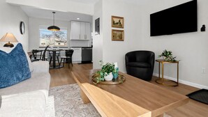 Una sala de estar moderna con sofá, mesa de centro y comedor con sillas, y una cocina al fondo.