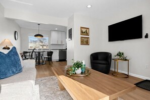 Ein modernes Wohnzimmer mit Sofa, Couchtisch und Essbereich mit Stühlen. Im Hintergrund ist eine Küche zu sehen.