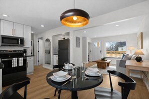 A modern kitchen with a dining area, featuring a black dining table, white plates, and a black chandelier. - Comfortable 1BR w/ In-Unit Laundry + WiFi | Ideal for Extended Stays (Eastpointe)